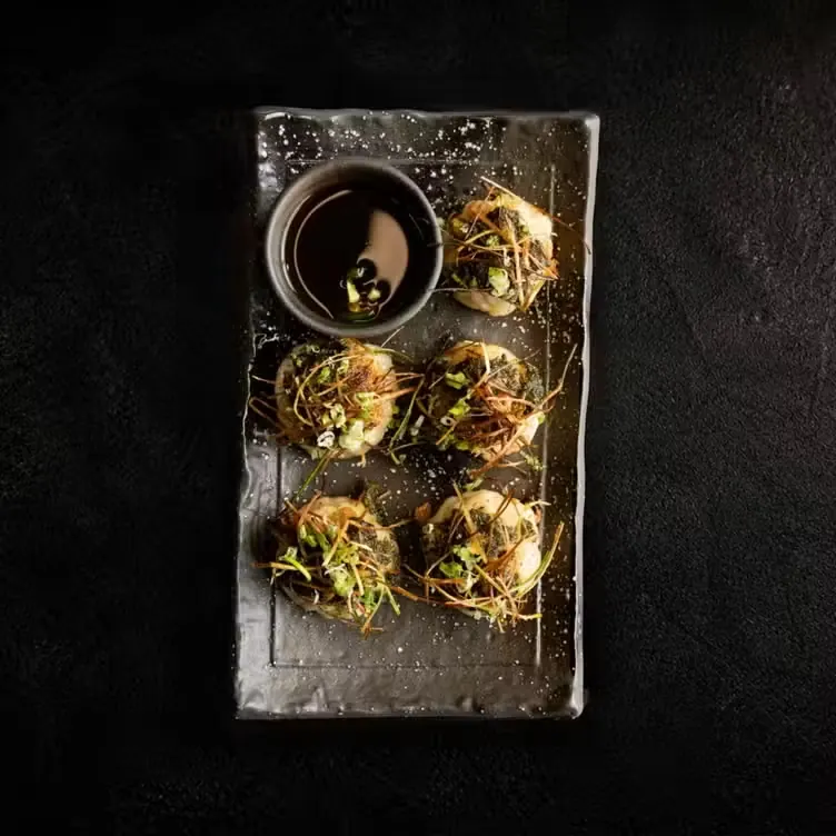 Crisped dumplings with dipping sauce on a dark plate